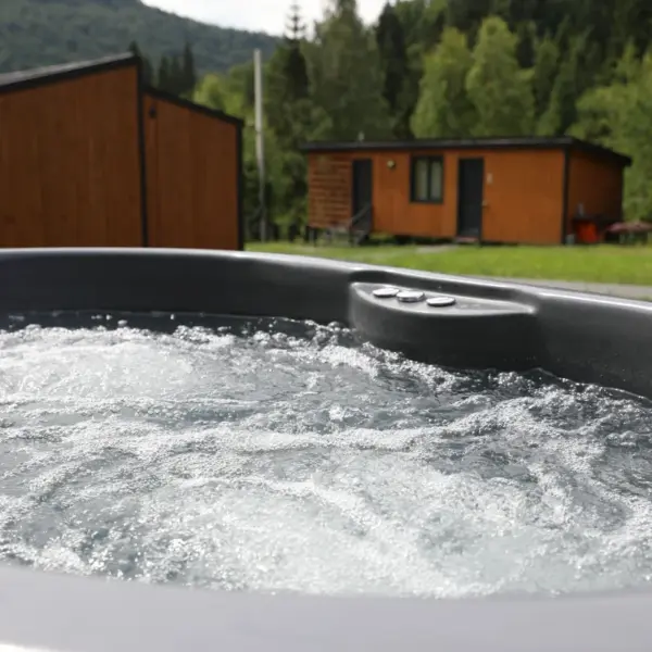 Bubbling outdoor hot tub on a deck with wooden cabins and forest in the background