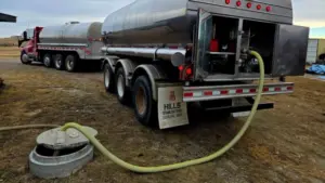 Water delivery tanker truck with hose connected to an underground cistern fill port in a rural yard