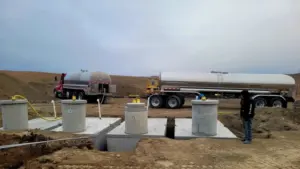 Two water tanker trucks filling newly installed underground cistern tanks at a construction site