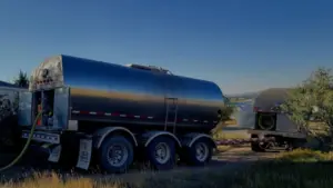 Water tanker truck parked at a scenic rural property with mountains and a lake at sunset
