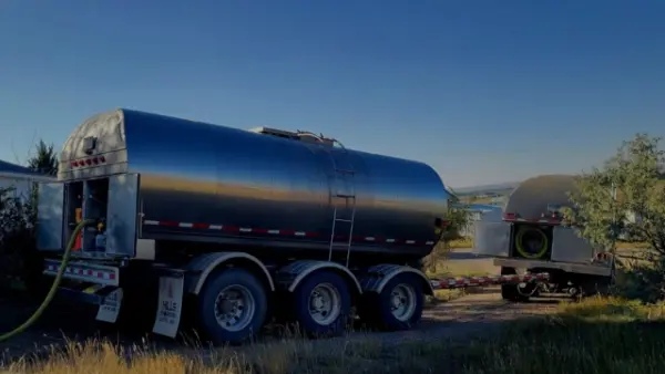Water tanker truck parked at a scenic rural property with mountains and a lake at sunset